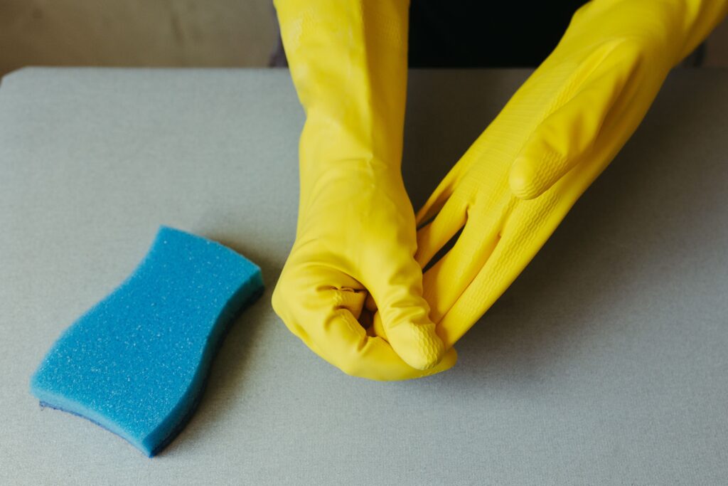 Sarung Tangan Karet Tebal: Pilihan Tepat di Berbagai Industri Close-up of hands wearing yellow gloves next to blue sponge on gray surface.
