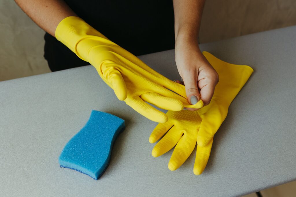 Individual putting on yellow rubber gloves with a blue sponge nearby.
